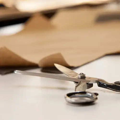 A pair of vintage-style scissors with metallic blades and black handles, resting on a white surface.